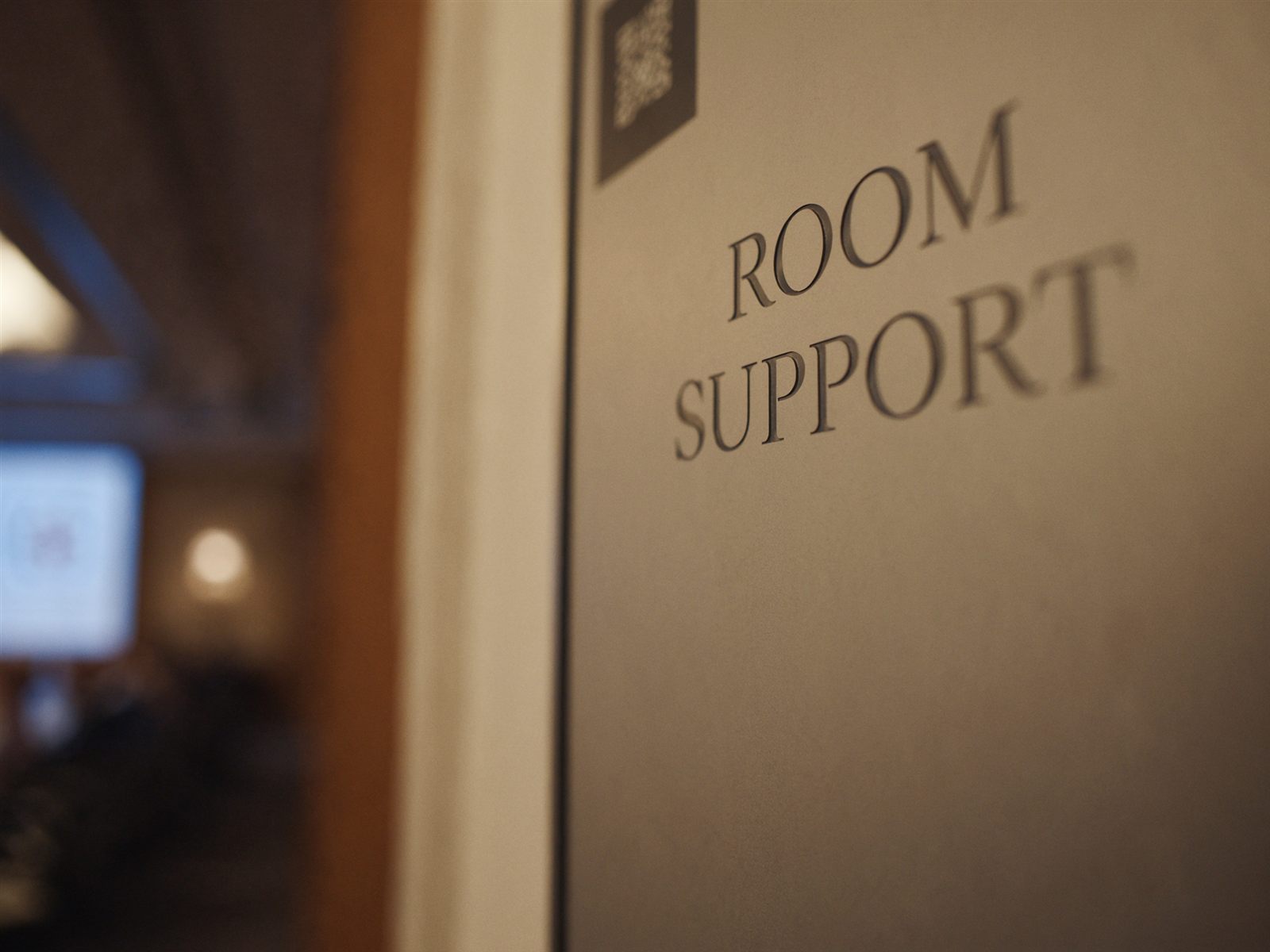 An elegant metal placard beside a conference room door reading ROOM SUPPORT with a QR code